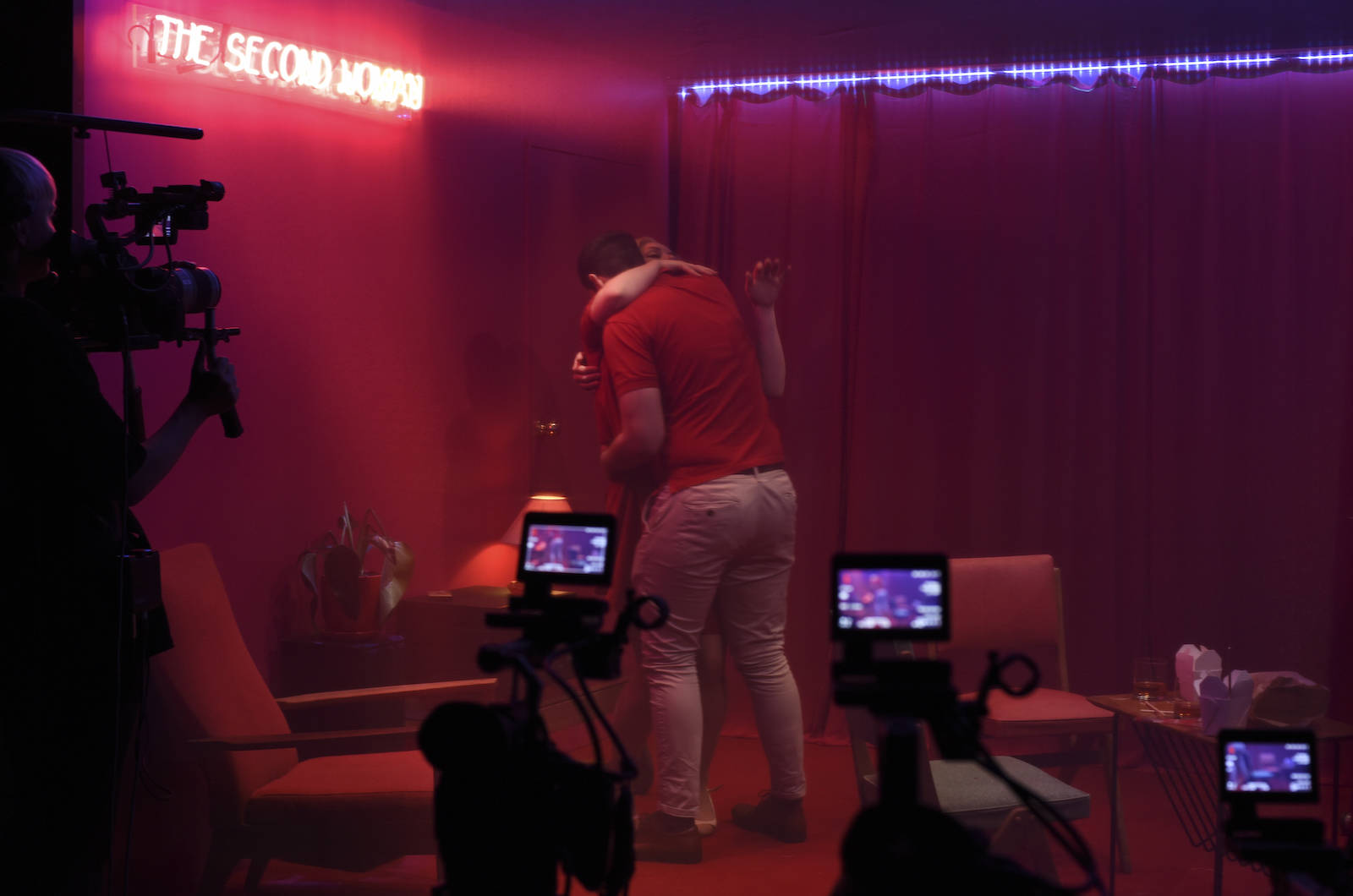 圖：《The Second Woman》舞台上，一座透著粉紅色光的房間，女子等著一名男子的來訪，房間右側是及地等高投影幕，同步上映著鏡頭內的另一種視野。
